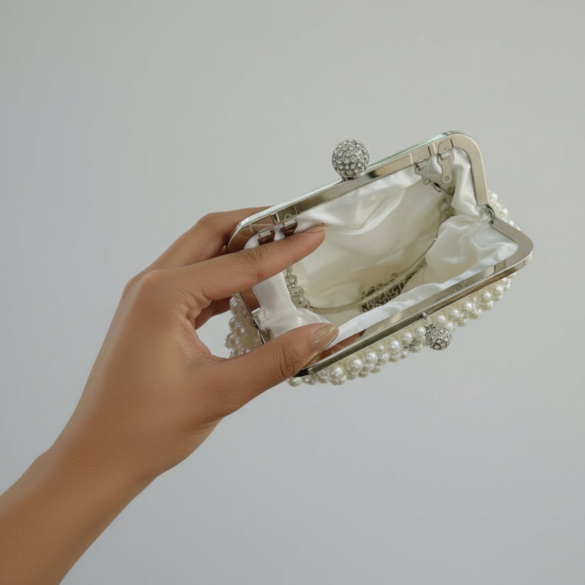 Hand holding a decorative clutch bag with pearls on a plain background