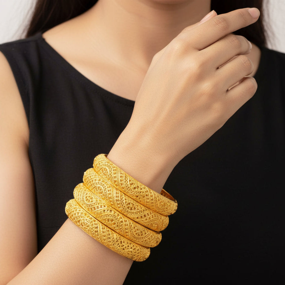 Gold bangles on a person's wrist with a plain background