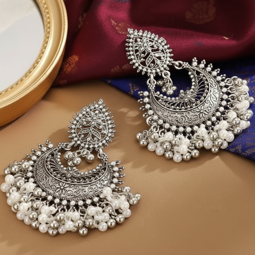 Ornate silver earrings with pearl-like beads on a fabric background
