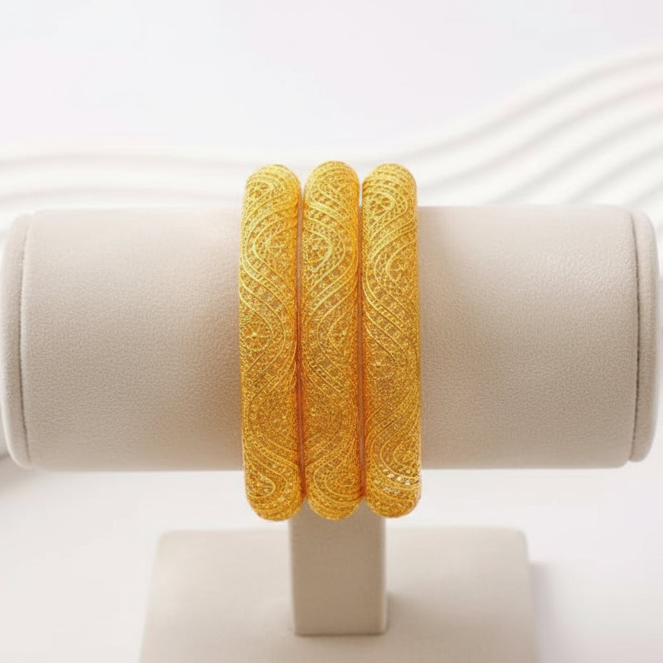 Three gold bangles on a white stand with a white background