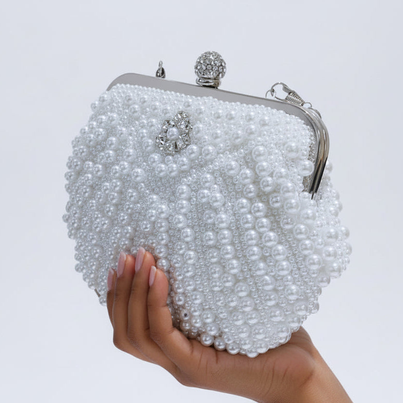 White pearl clutch held by a hand against a light gray background