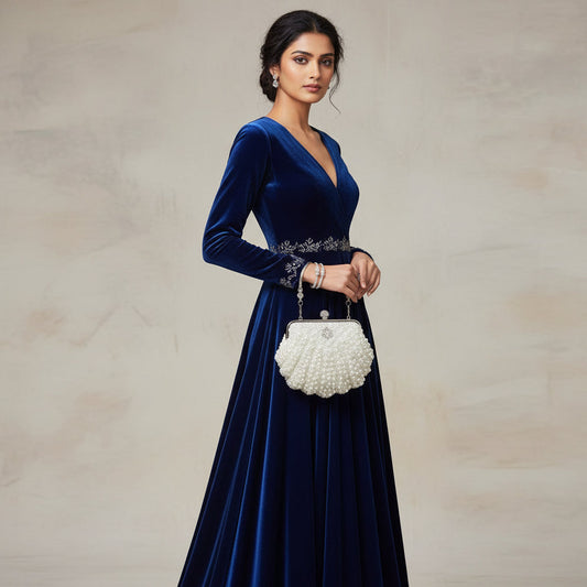 Woman in a blue velvet dress holding a white handbag against a neutral background