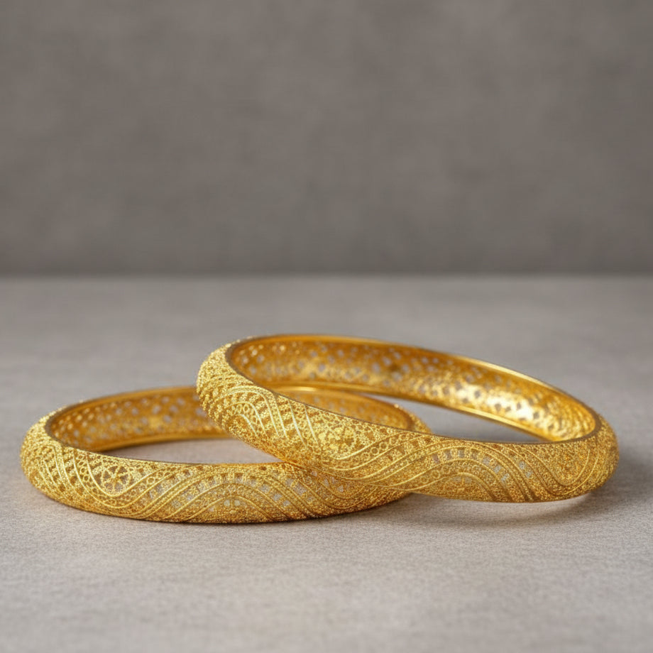 Two gold bangles with intricate designs on a gray background