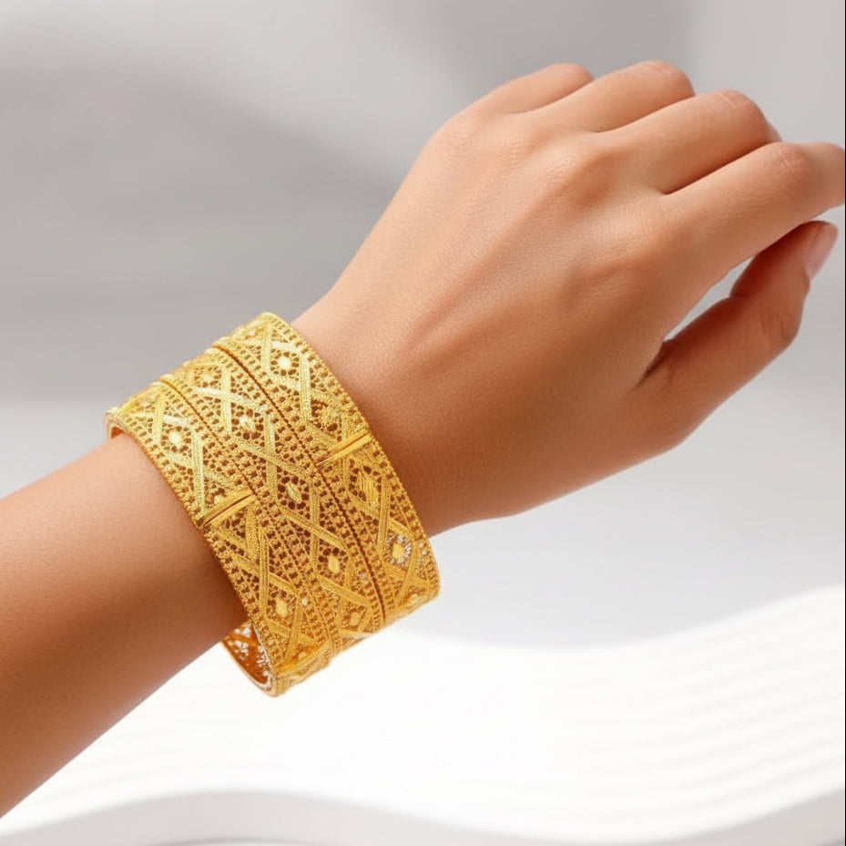 Gold bracelet with intricate designs held by a hand on a white background